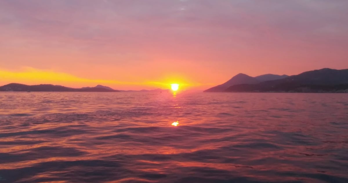 A pink sky over the sea as the sun sets between two lines of islands, seen from the water