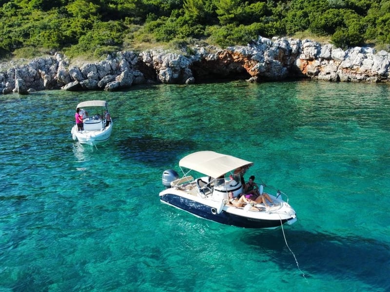 The Fisher 20 at anchor with its sun canopy up, in clear turquoise water off a rocky shore