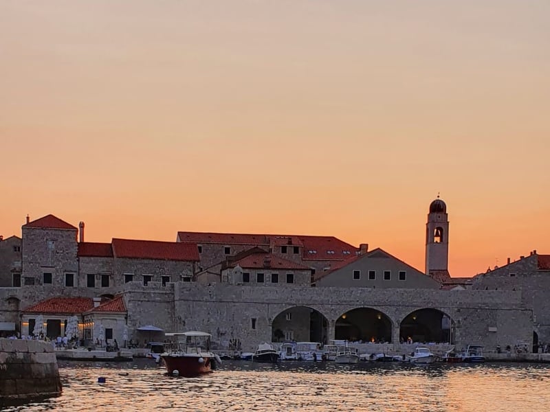 Dubrovnik’s old harbour and bell tower in golden light, seen from the back of a sunset boat