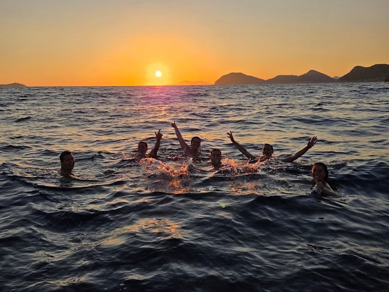 Guests swimming in the sea at sunset, some with their arms in the air, islands on the horizon