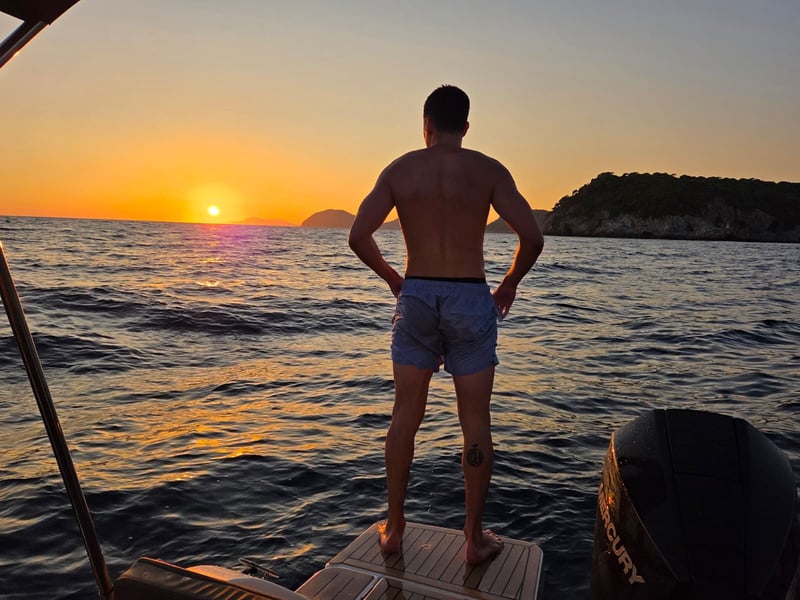 A guest standing on the boat’s swim platform, watching the sun set between two islands