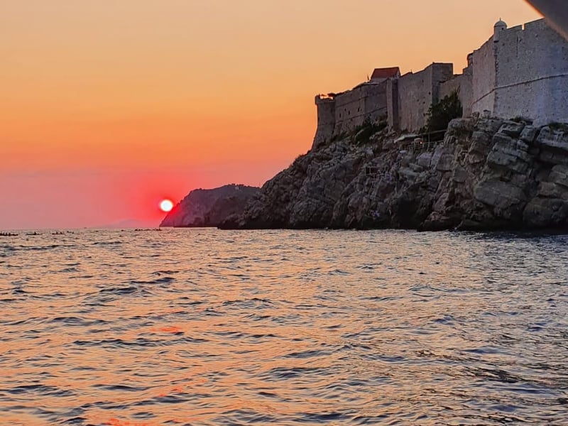The sun dropping into the sea beside Dubrovnik’s fortress walls, seen from a boat